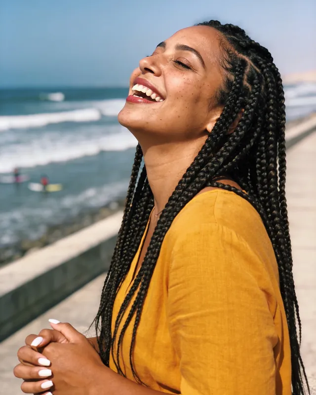 Imagen referencial: mujer con trenzas largas riendo junto al mar
